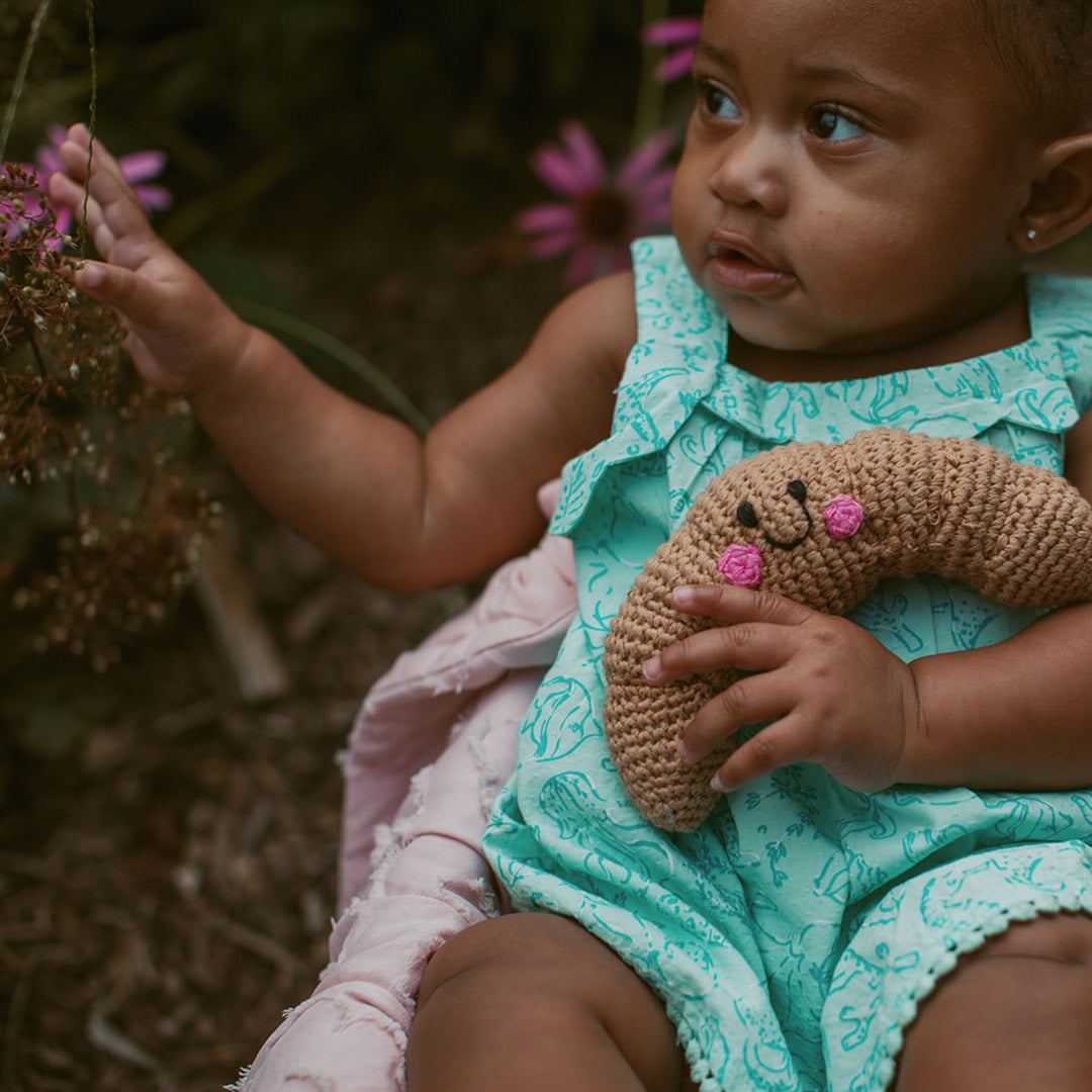 girl holding organic cotton crochet croissant toy food rattle