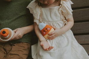 Two children holding crochet fall toys one in a white dress and the other in a green shirt.