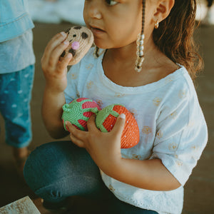 Girl pretending to eat crochet cookie and holding fruit soft toys