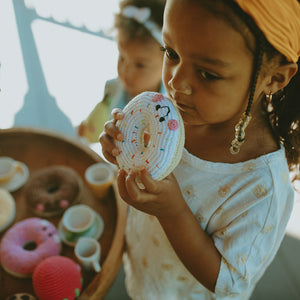 Girl pretending to eat crochet handmade white doughnut with sprinkles soft toy