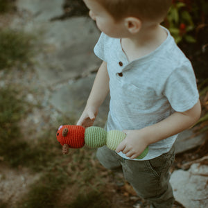 Boy holding green and red handmade crochet caterpillar toy.