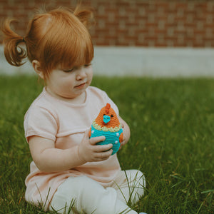 Girl sitting in grass, holding turquiose and orange baby chick toy.